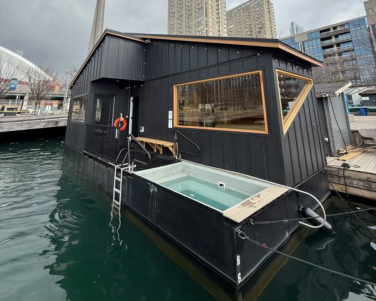 The floating sauna on the Toronto harbourfront, with the plunge tub on the deck and the CN Tower behind